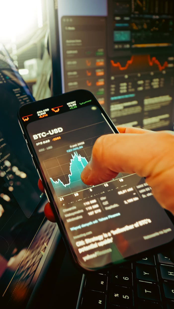 home-services-03 A hand holds a smartphone displaying BTC-USD chart amidst digital trading screens, highlighting crypto finance.